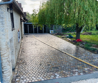 Travaux en cours sur terrasse en pavés grès à côté d'un bâtiment en pierre